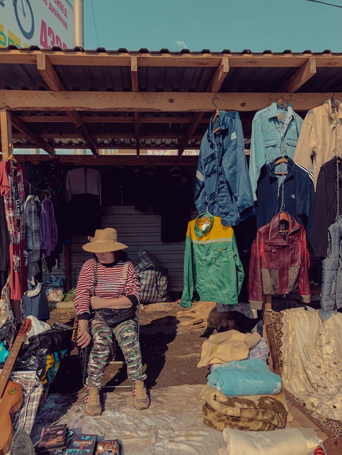 A street market stall displaying colorful vintage clothes and a seated vendor, conveying a bohemian vibe.
